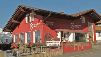 Bâtiment rouge du restaurant Kainer avec balcon en bois et espace extérieur accueillant