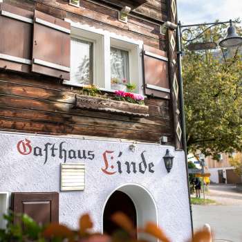 Façade de l'Gasthaus Linde avec une construction en bois rustique et des volets décorés de fleurs.