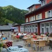 Terrasse ensoleillée du restaurant avec tables couvertes, parasols et vue sur les Alpes.
