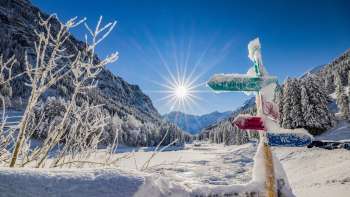 Panneau indicateur enneigé dans le domaine de ski de fond de Valüna - Steg avec un soleil d'hiver radieux