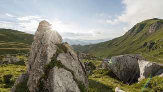 Lever de soleil derrière des formations rocheuses dans la vallée verdoyante de la Naaftal au Liechtenstein, entourée de douces collines et d'un paysage montagneux
