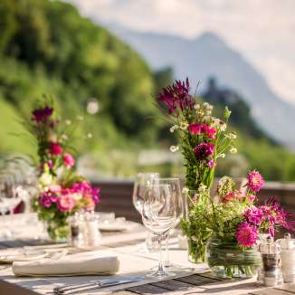 Une table élégante avec des arrangements floraux sur une terrasse avec vue sur les Alpes - le décor parfait pour des fêtes ou des dîners romantiques au Liechtenstein