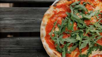 Pizza fraîche à la sauce tomate et à la roquette, servie sur une table rustique en bois