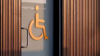 Symbole orange de fauteuil roulant sur une porte vitrée indiquant des toilettes accessibles, avec des boiseries en arrière-plan.