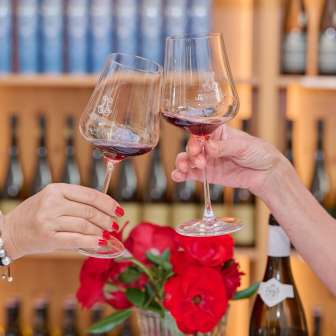Deux femmes trinquent avec du vin rouge à la Hofkellerei Liechtenstein, avec en arrière-plan des étagères remplies de vins fins.