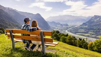 Couple sur un banc en bois avec vue sur la vallée du Rhin et les montagnes.
