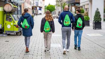 Quatre jeunes avec des sacs à dos verts traversent la zone piétonne de Vaduz – sur le FoodTrail Vaduz Quatre jeunes avec des sacs à dos verts traversent la zone piétonne de Vaduz – sur le FoodTrail Vaduz