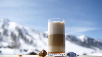 Verre de latte macchiato sur un plateau en bois avec les montagnes enneigées en toile de fond