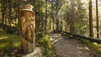 Figurine en bois avec lanterne au « sentier des légendes walsers » dans la lumière mystique de la forêt