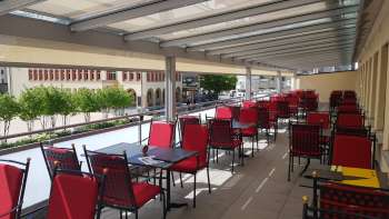 Terrasse ensoleillée avec des chaises rouges et des tables nappées de blanc Terrasse ensoleillée avec des chaises rouges et des tables nappées de blanc