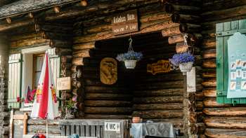 Entrée de la cabane : entrée rustique de la refuge Gafadurahütte avec façade en bois, fleurs multicolores et panneau d'information.