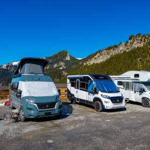 Plusieurs campeurs et camping-cars sur un emplacement dans les montagnes du Liechtenstein sous un ciel bleu éclatant