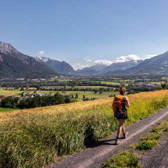 Une femme se promène sur un chemin de terre avec une vue panoramique sur la vallée du Rhin au Liechtenstein