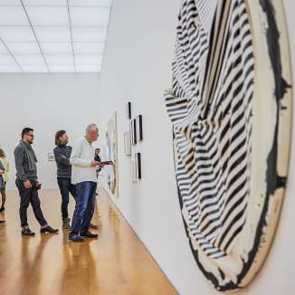 Les visiteurs contemplent des œuvres d'art moderne dans une galerie du Kunstmuseum Liechtenstein à l'architecture lumineuse et au sol en bois.