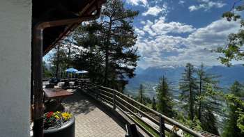 Terrasse ensoleillée de l'auberge de montagne Matu avec vue sur la vallée du Rhin et le paysage montagneux environnant.