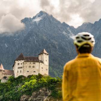 Un cycliste casqué contemple l'imposant château de Gutenberg sur fond de montagnes dramatiques à Balzers - Tour culturel à vélo au Liechtenstein