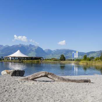 Espace de baignade proche de la nature avec du sable, du bois flotté et une vue sur les Alpes liechtensteinoises dans le parc de loisirs de Grossabünt.