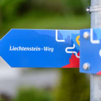 Panneau indicateur bleu avec l'inscription « sentier du Liechtenstein » au design moderne.