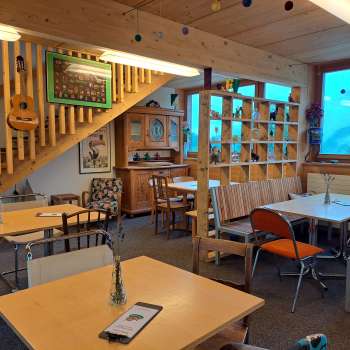 Salle de restaurant avec baie vitrée et décoration - Tables et chaises dans un espace ouvert avec de grandes fenêtres et vue sur l'extérieur verdoyant.