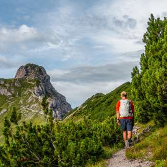 Randonneurs sur un sentier étroit à travers les pins de montagne à Malbun, Liechtenstein, avec vue sur des sommets rocheux