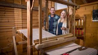 Un couple regarde un métier à tisser historique en état de marche au musée Walser de Triesenberg au Liechtenstein, entouré de boiseries.