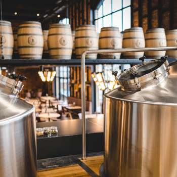 Vue d'une brasserie moderne avec des cuves en inox brillantes et des fûts en bois empilés en arrière-plan.