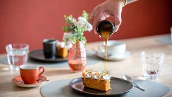 Dessert nappé de sauce caramel, avec en arrière-plan des tasses de café et une décoration de table stylée