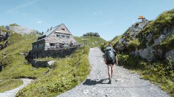 Une randonneuse avec un sac à dos se dirige sur un sentier de montagne vers le refuge Pfälzerhütte dans les Alpes liechtensteinoises.
