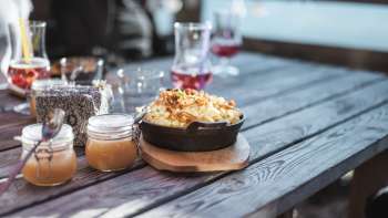 Spécialité régionale « Käsknöpfle » avec compote de pommes sur une table en bois devant un décor alpin