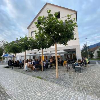 Terrasse animée du St. Martins Pub am Platz avec des arbres ombragés et des clients attablés.