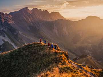 Groupe de coureurs de trail sur une crête près de Malbun, Liechtenstein, dans la lumière chaude du coucher de soleil avec vue sur les Alpes.