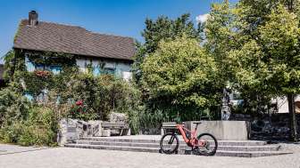 vélo électrique à travers le Liechtenstein - Entre nature, culture et plaisirs de la table vélo électrique rouge devant un bâtiment historique du Liechtenstein, entouré d'arbres et de fontaines, point de départ idéal pour une balade à vélo à travers le pays.