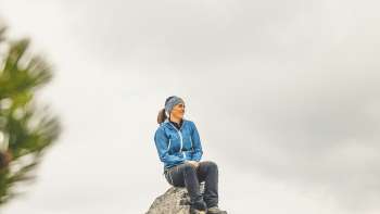 Rosaria Michaela Ackermann est assise sur une pierre dans les montagnes du Liechtenstein et regarde au loin.