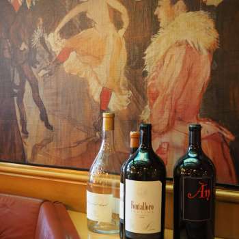 Trois bouteilles de vin devant une fresque artistique à la Brasserie Burg - l'élégance méditerranéenne rencontre le flair artistique.
