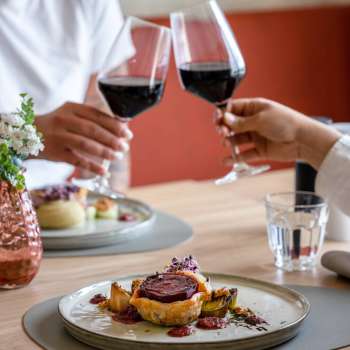 Deux personnes trinquent avec du vin rouge, au premier plan un plat principal soigneusement préparé