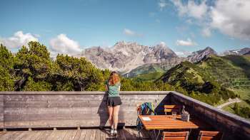 Une randonneuse contemple un impressionnant panorama alpin depuis une terrasse en bois près de la terrasse panoramique.