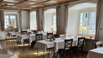 Salle de restaurant claire et classique avec des nappes blanches et un sol en bois.