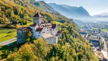Le château de Vaduz dans un décor alpin automnal avec vue sur la vallée du Rhin