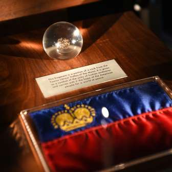 Pièce d'exposition dans le Trésor du Liechtenstein : drapeau du Liechtenstein avec couronne dorée et sphère en verre avec pièce historique trouvée