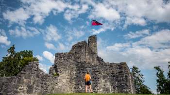 Une randonneuse se tient devant les ruines imposantes du château de Schellenberg sous un ciel bleu