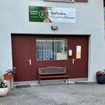 Entrée de la boutique de la ferme Aeulehof avec portail rouge, banc et décoration florale à Triesen, Liechtenstein.