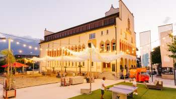 Place de l'hôtel de ville de Vaduz dans une ambiance de soirée lors d'un jour de marché animé avec la foule, les stands de vente et un éclairage d'ambiance.