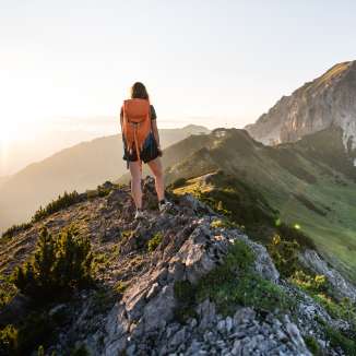 Une femme avec un sac à dos admire le lever du soleil lors d'une randonnée à Malbun avec vue sur le paysage de montagne.