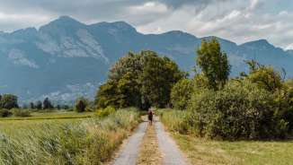Randonneurs sur un chemin de terre au milieu d'une nature verdoyante avec vue sur l'imposant décor montagneux entre Schaanwald et Ruggell.