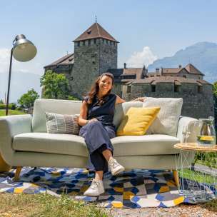 Femme assise sur un canapé avec vue sur le château de Vaduz et les montagnes du Liechtenstein, ambiance moderne en plein air avec décoration
