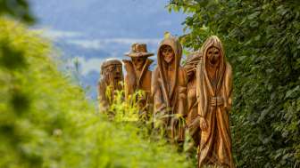 Vue détaillée de figures en bois sculptées dans une représentation mystique sur le sentier des légendes walser à Triesenberg, entouré d'une nature verdoyante