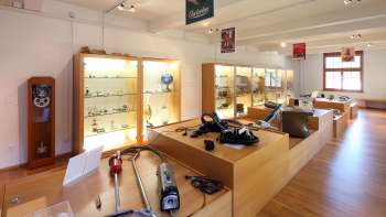 Exposition au Musée Lawena avec des vitrines, de vieux appareils électroménagers et une collection historique d'aspirateurs.