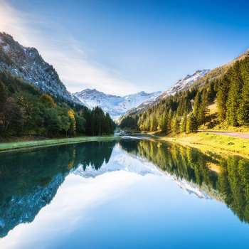 Lac Gänglesee à Steg avec reflet de la montagne, entouré de forêt, rayons de soleil sur la pente.