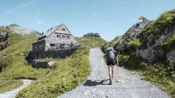 Une randonneuse avec un sac à dos se dirige sur un sentier de montagne vers le refuge Pfälzerhütte dans les Alpes liechtensteinoises.