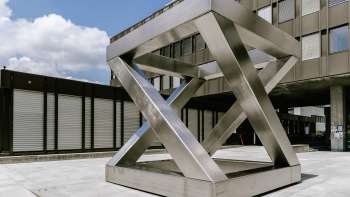 Sculpture géométrique Z-Würfel de Georg Malin à Vaduz - surfaces en acier inoxydable décalées en forme de cube sur une place publique.